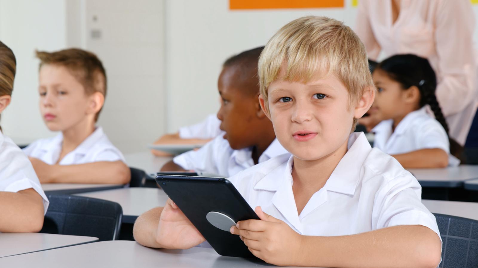 bambino biondo in classe utilizza tablet